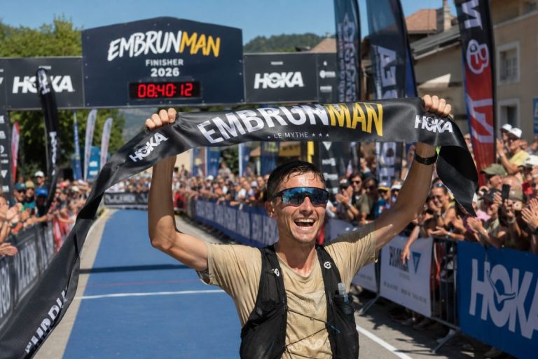 Triathlète franchissant la ligne d’arrivée de l’Embrunman 2026 à Embrun, bras levés devant le public.