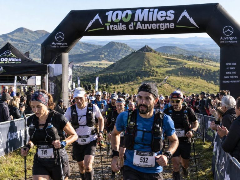 Départ du 100 Miles Trails d’Auvergne avec un groupe de traileurs sous l’arche de course, dans un décor volcanique et montagneux auvergnat.