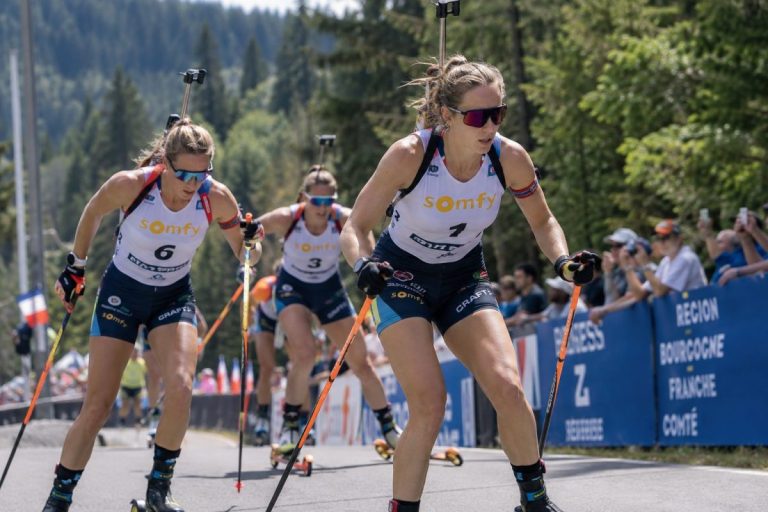Biathlètes féminines en pleine course de ski-roues lors du Summer Tour de biathlon d’Arçon 2026, sur une route bordée de forêt et de spectateurs.