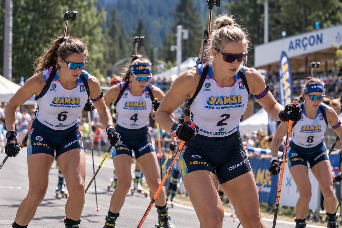 Biathlètes féminines en pleine course de ski-roues lors du Summer Tour d’Arçon 2026, avec carabines sur le dos, tenues de compétition et spectateurs au bord du parcours.