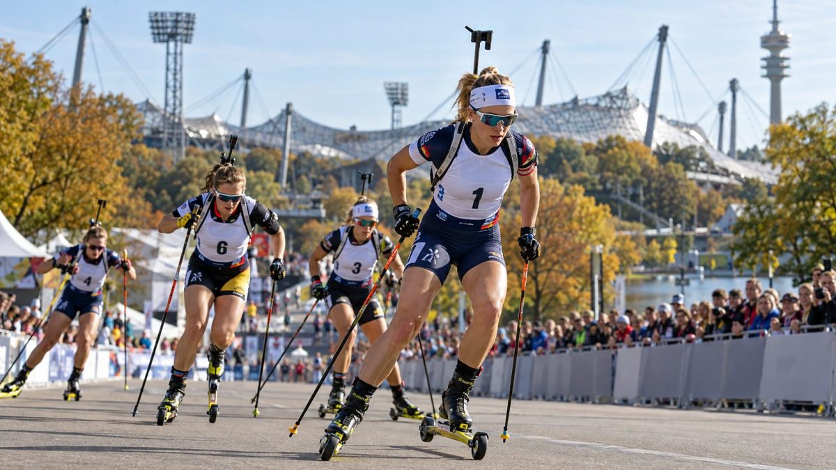 Biathlètes en pleine course de ski-roues lors du Loop One Festival 2026 à Munich, devant le stade olympique et les spectateurs de l'Olympiapark.