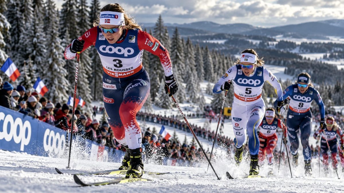 Fondeurs en pleine course lors du Tour de Ski 2027 aux Rousses, sur une piste enneigée du Jura avec le public en bord de parcours.