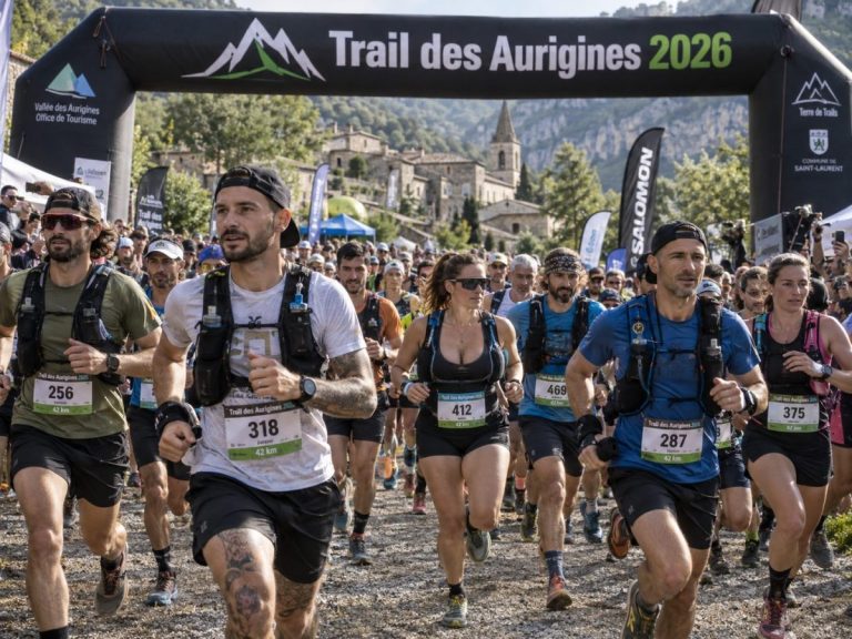 Départ du Trail des Aurigines 2026 avec des coureurs et coureuses portant des dossards et des tenues de trail, sur un chemin caillouteux au pied d'un village de montagne.